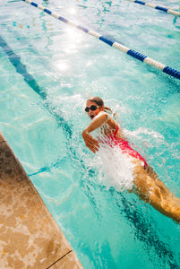 woman swimming with goggles on, wearing a red swimsuit.